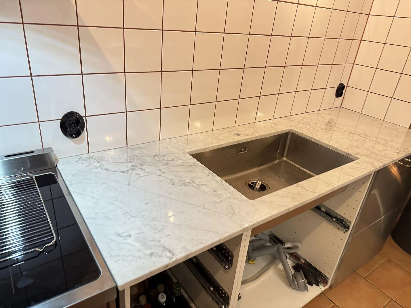 Køkkenbordplade i Carrara C-marmor, poleret, med rostfri vask og hvid kakelvägg i ett køkken i Borrby.