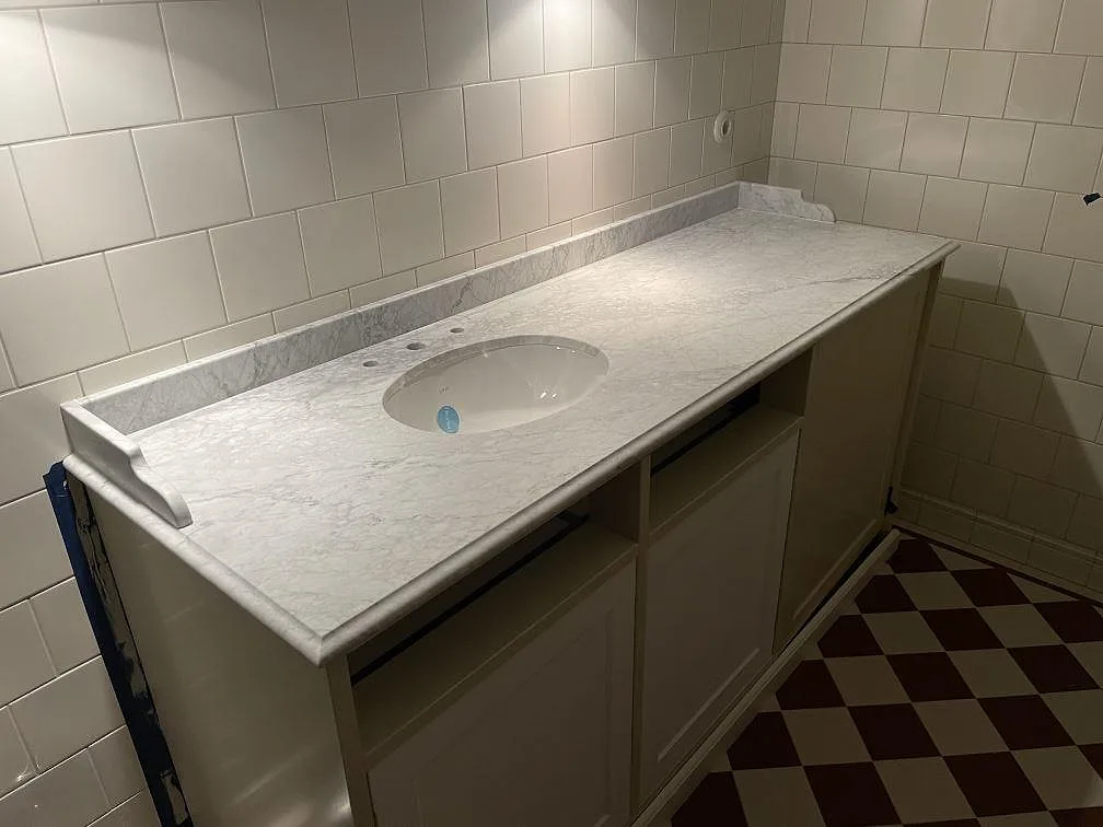 Kommodskiva i hvid Carrara C-marmor, mat overflade, med underlimmat ovalt tvattstall og uppvikt stankkant i ett badeværelse i Bromma.