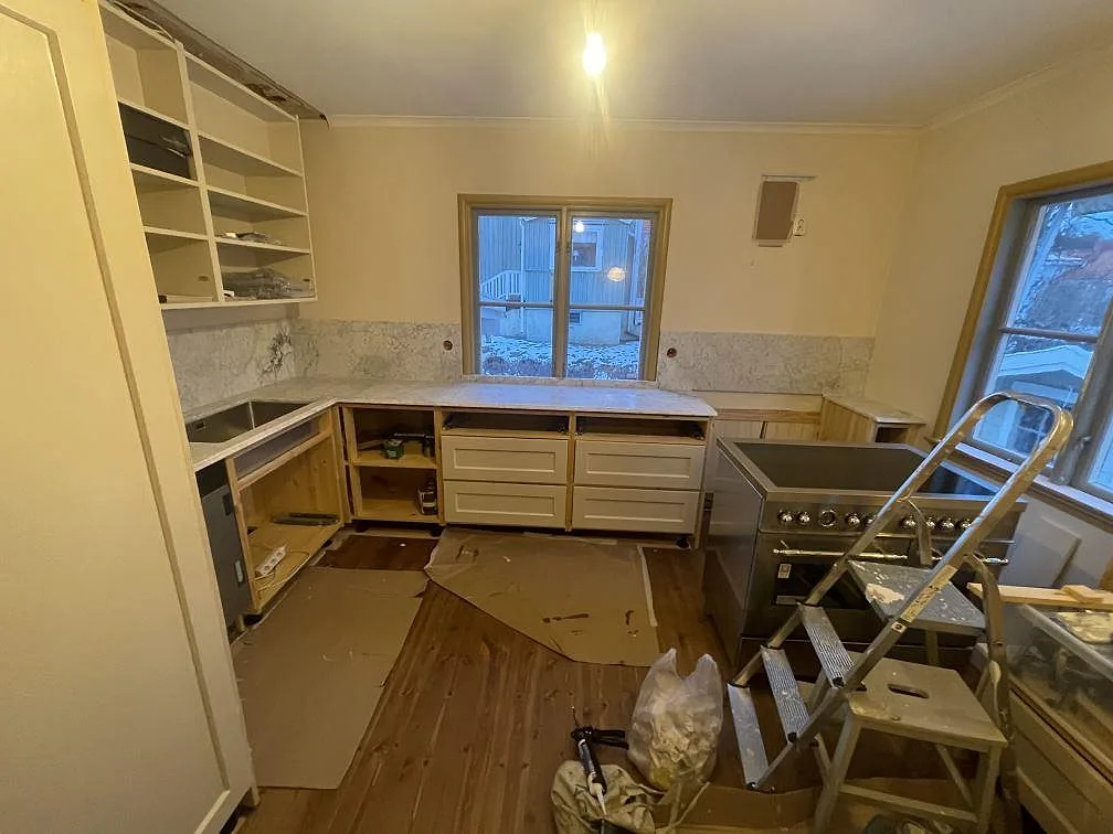 Køkkenbordplade i hvid Carrara C-marmor, mat, i ett L-format køkken i Bromma med heltäckande marmorstänkskydd og fristående komfur under montering.