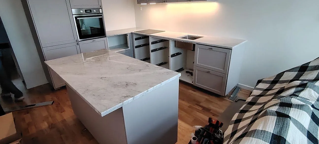 Køkkenbordplade i Carrara C marmor, poleret 30 mm, med stor køkkenø og lys väggbänk under montering i Danderyd.