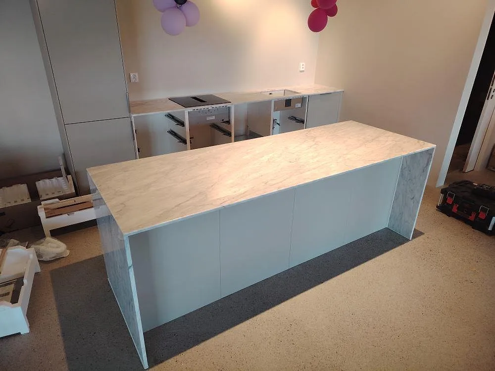 Køkkenø og bakre køkkenbordplade i hvid Carrara C marmor, 20 mm poleret, under montering i ett køkken i Ekolsund.