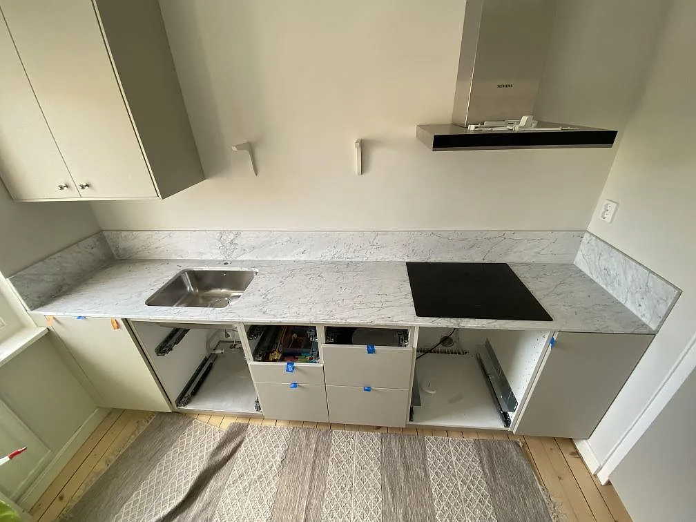 Køkkenbordplade i hvid Carrara C-marmor, mat overflade, med underlimmad rostfri vask og infälld induktionshäll i ett køkken under montering i Göteborg.