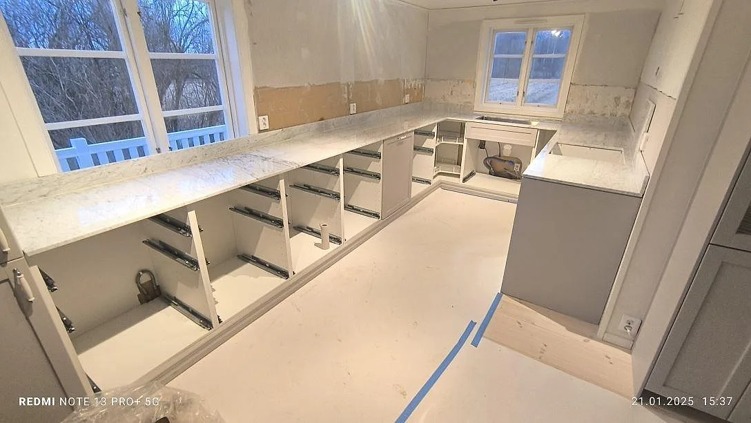 Køkkenbordplade i hvid Carrara C-marmor, poleret, med lang bänkyta og køkkenø i ett køkken under montering i Hallsberg.