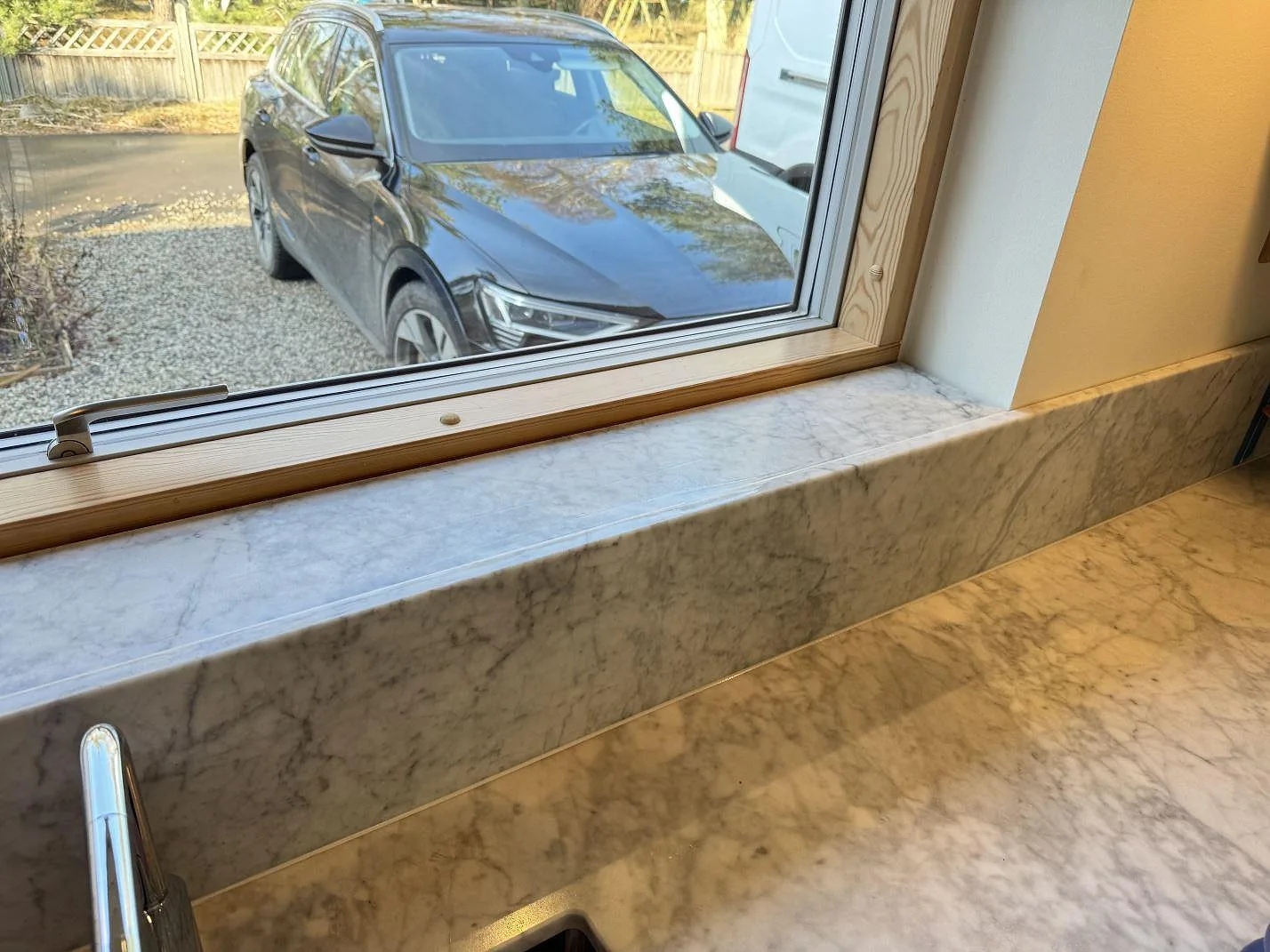 Køkkenbordplade i mat Carrara C marmor med uppvikt stänkkant og vindueskarm vid ett köksfönster i Höllviken.