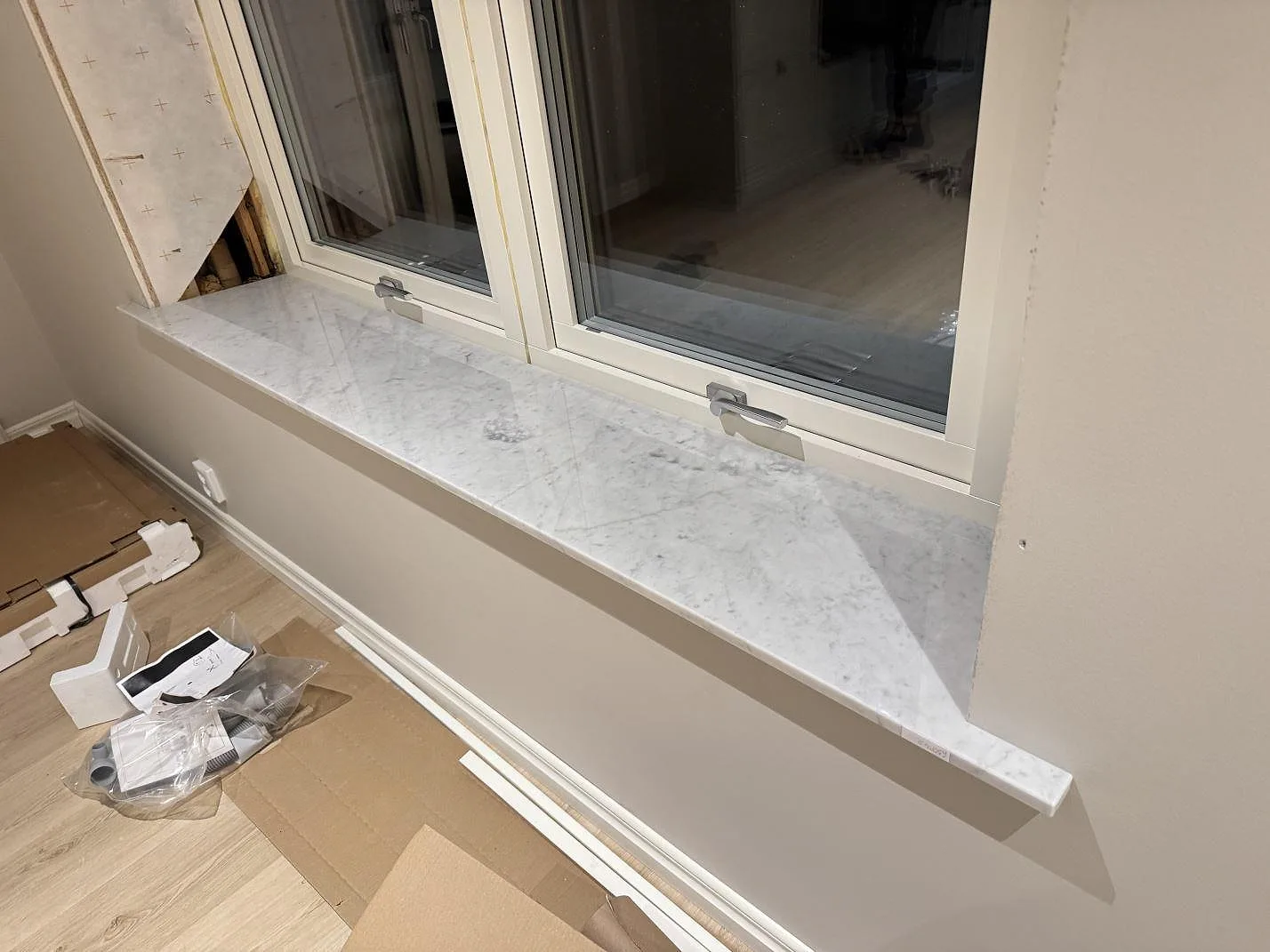 Poleret vindueskarm i Carrara C marmor med grå åretegning vid ett vindue i Kristianstad, fotograferad under montering.
