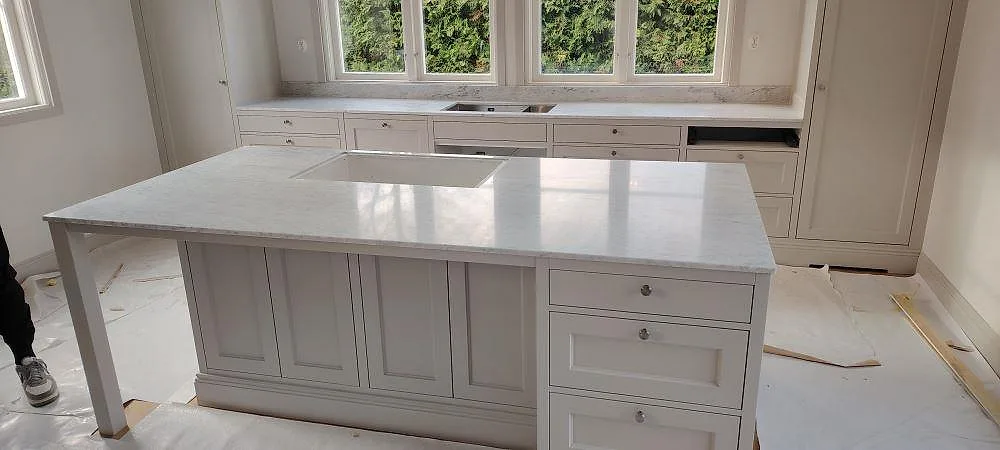 Køkkenø og Bordplader i mat Carrara C marmor, 20 mm, med synligt udskæring i köksön i ett ljust køkken i Lidingö.