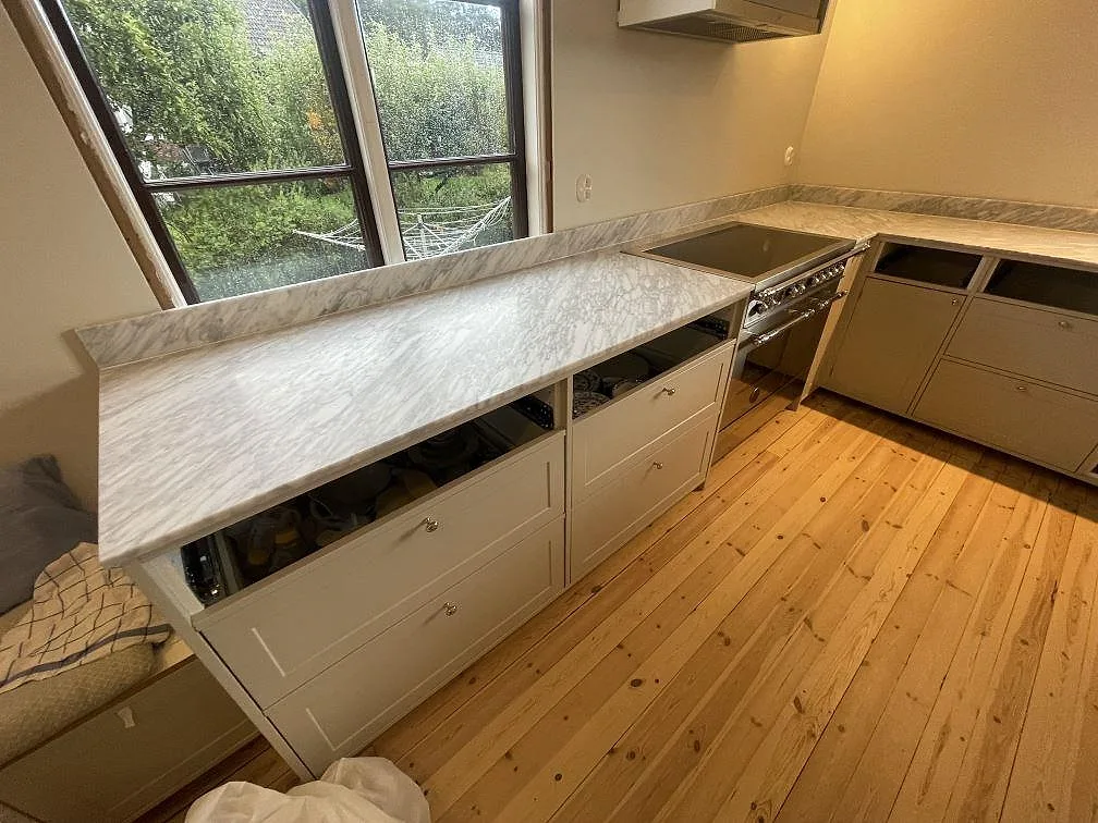 Køkkenbordplade i Carrara C marmor, mat, med uppvikt stänkkant og komfur i ett køkken i Linköping.