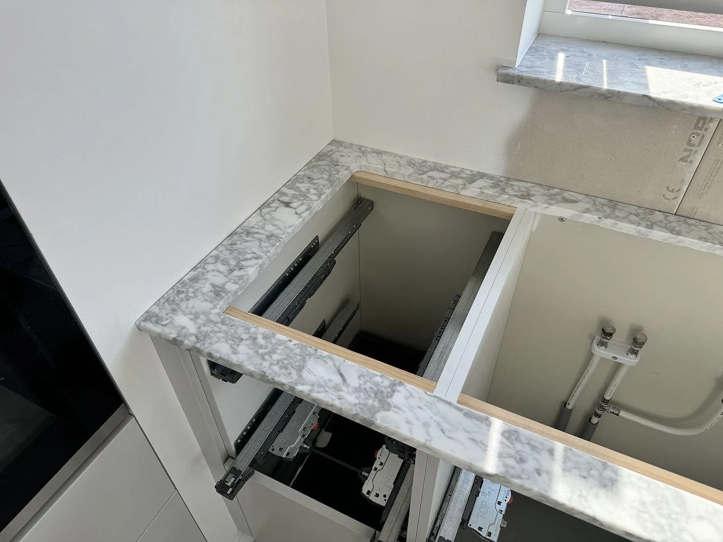 Poleret Bordplade i Carrara C marmor rundt om en öppen badrumskommod med fönsterljus i Lomma.