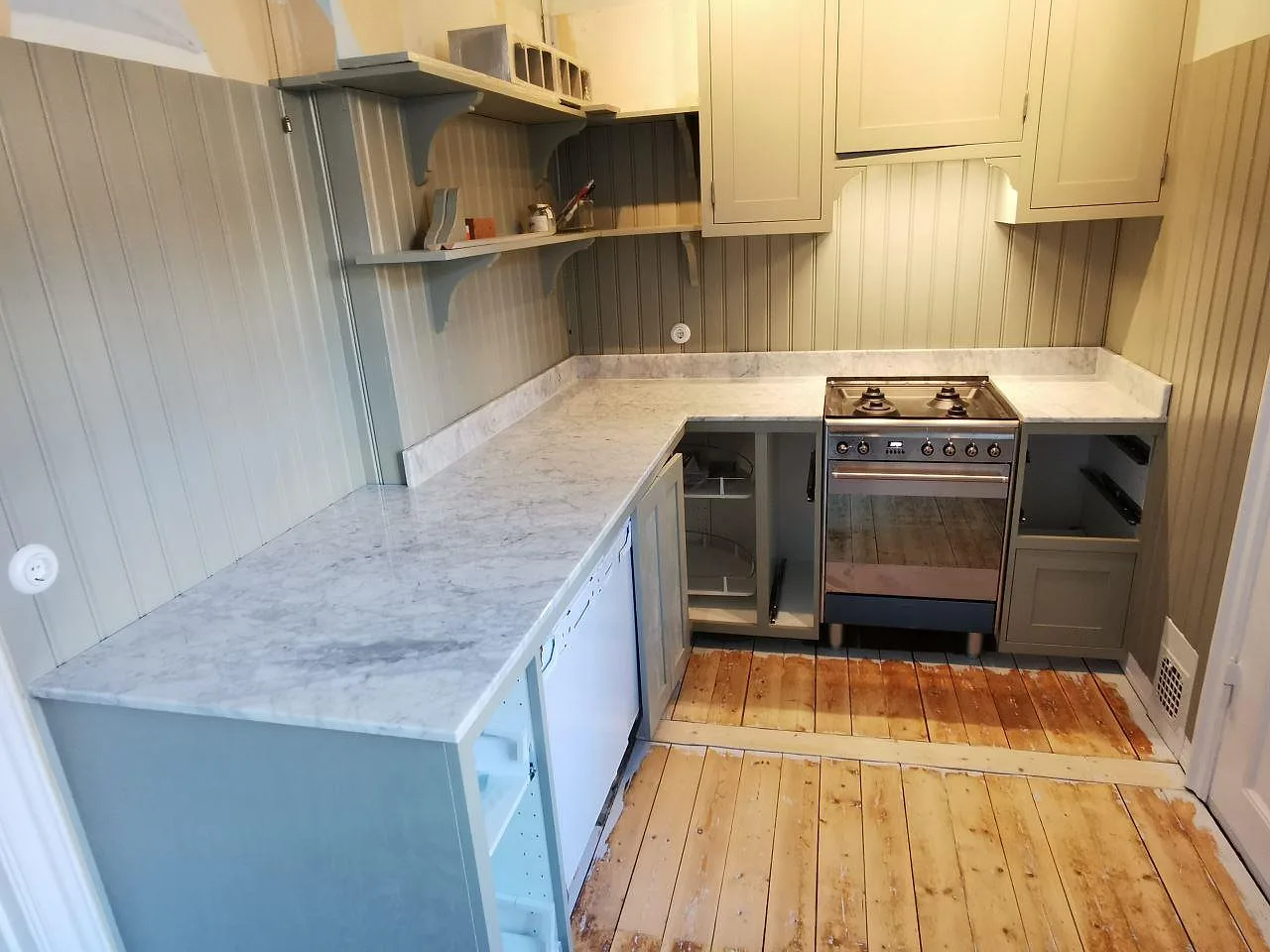 Køkkenbordplade i Carrara C, poleret hvid marmor med grå åretegning, i ett litet køkken i Malmö med salviegrön pärlspont, greppfria shakerluckor og en fristående rostfri gasspis.