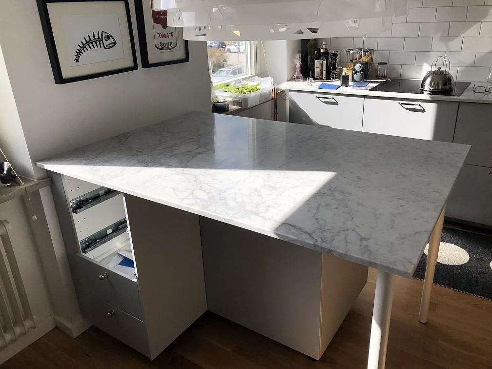 Køkkenbordplade i hvid Carrara C marmor, mat, monteret som køkkenø med frukostbar i ett køkken i Malmö, sedd under montering.