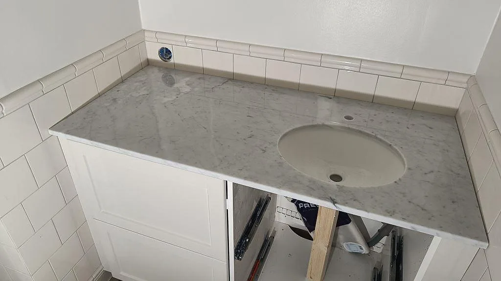 Badrumsbänkskiva i poleret Carrara C marmor med rund tvättställsskål og lys kakelvägg i Malmö.