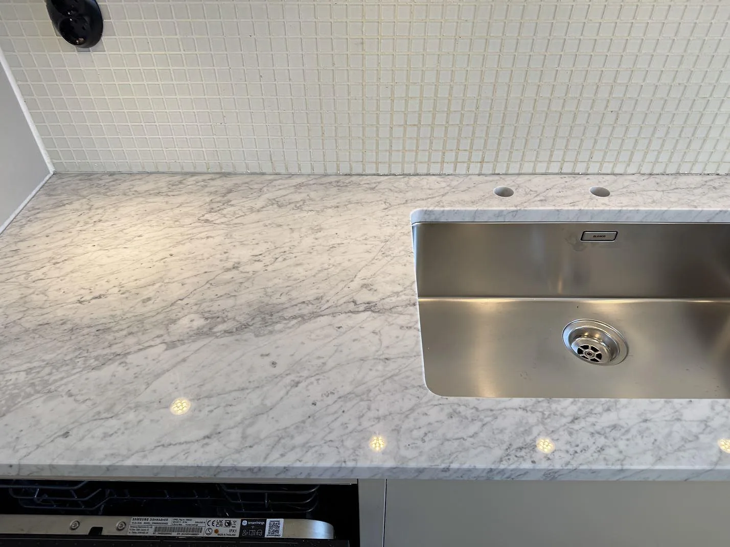 Køkkenbordplade i poleret Carrara C-marmor med rostfri vask og vitt mosaikkakel i ett køkken i Malmö.