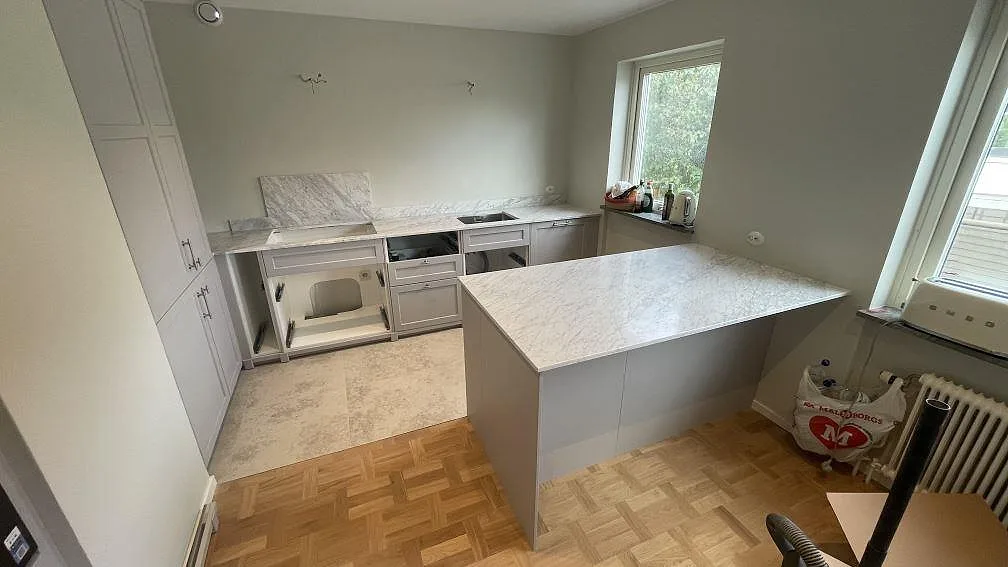 Mat køkkenbordplade og køkkenø i Carrara C marmor i ett køkken under montering i Malmö.