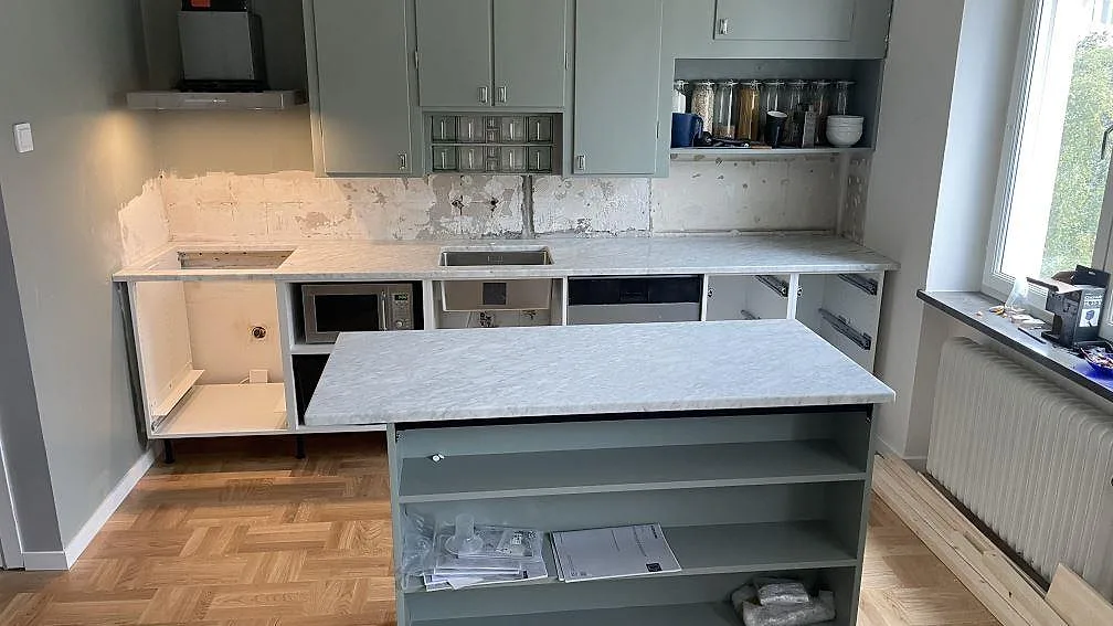 Køkkenbordplade og køkkenø i mat Carrara C-marmor i ett køkken under montering i Malmö.
