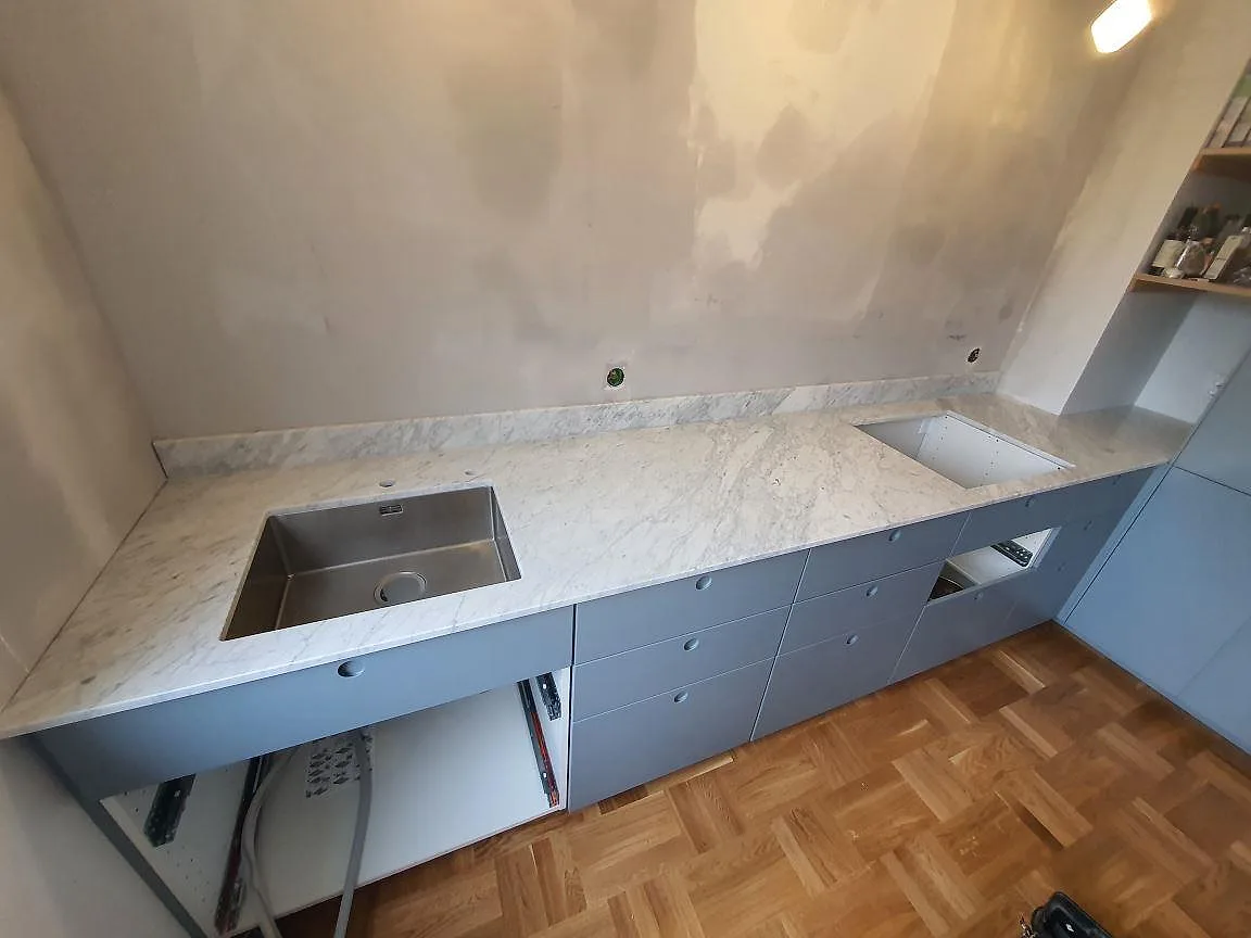 Køkkenbordplade i hvid Carrara C marmor, mat overflade, med underlimmad rostfri vask og uppvikt stänkkant i ett køkken i Nacka.