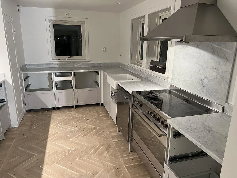Køkkenbordplade i mat Carrara C marmor med stänkkant og stenpanel bag spisen i ett køkken under montering i Österskär.