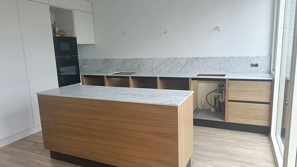 Køkkenbordplade og køkkenø i hvid Carrara C-marmor med grå åretegning, monteret på ekstommar med stænkplade i samme marmor, i ett køkken i Rødovre.