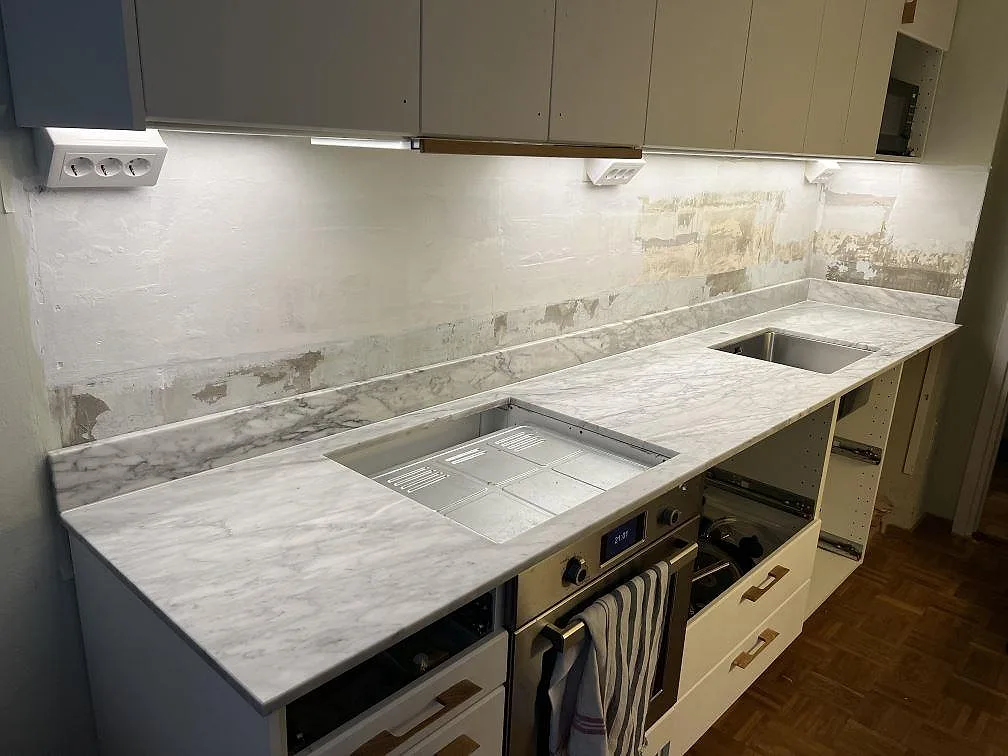 Køkkenbordplade i hvid Carrara C marmor, mat, med matchande stænkplade längs arbetsytan i ett køkken i Solna.