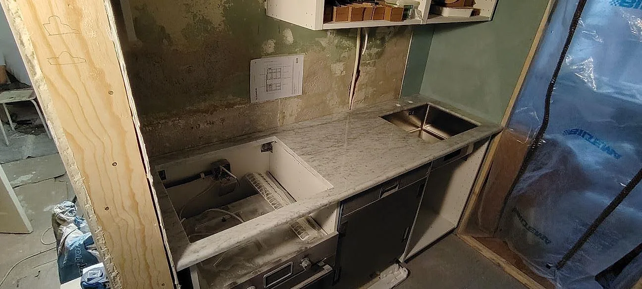 Poleret køkkenbordplade i 30 mm Carrara C marmor i ett køkken under montering i Stockholm, med lang bänksträcka og öppna skabe.