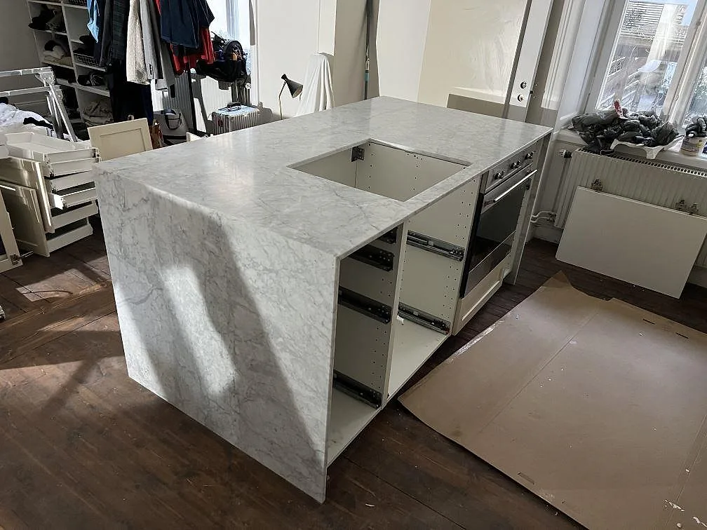 Køkkenø og køkkenbordplade i mat Carrara C-marmor, 20 mm, med neddraget sidostycke og förberedd öppning i ett køkken i Stockholm.
