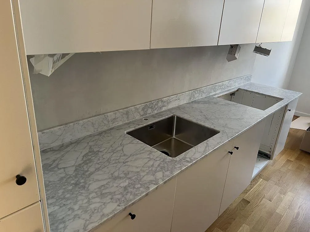 Køkkenbordplade i Carrara C marmor, mat, med vask, hällöppning og låg stänkkant i ett køkken i Stockholm.