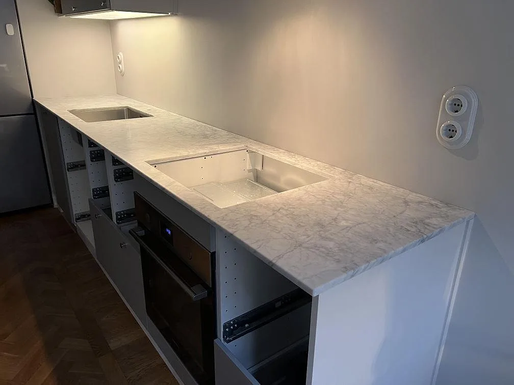 Lige køkkenbordplade i mat Carrara C marmor, 20 mm, med vask og hälluttag på öppna köksstommar i Stockholm.