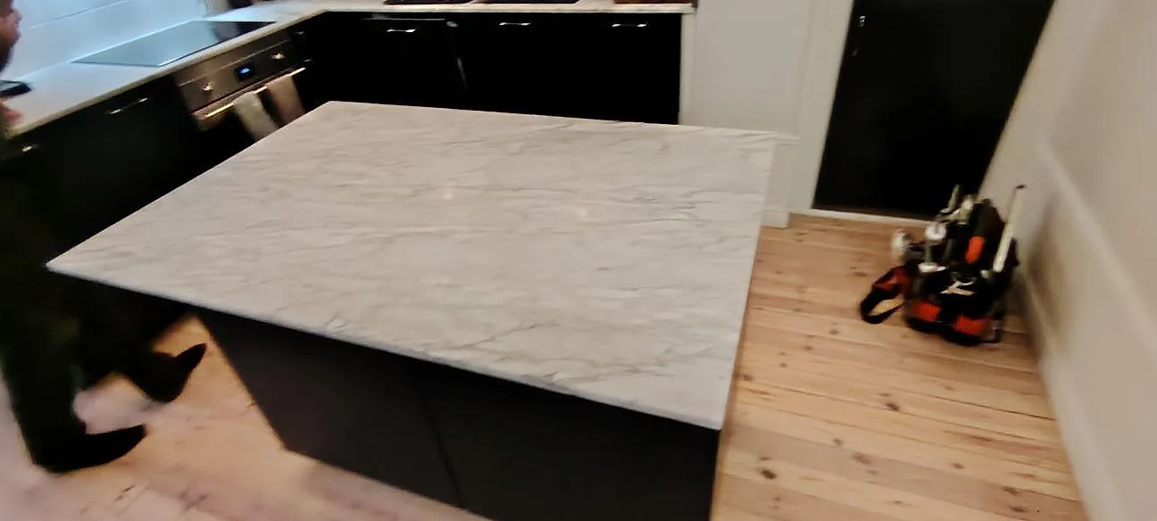 Køkkenbordplade og køkkenø i mat Carrara C marmor i 20 mm, med tydlig grå åretegning mot mørke köksluckor i Stockholm.