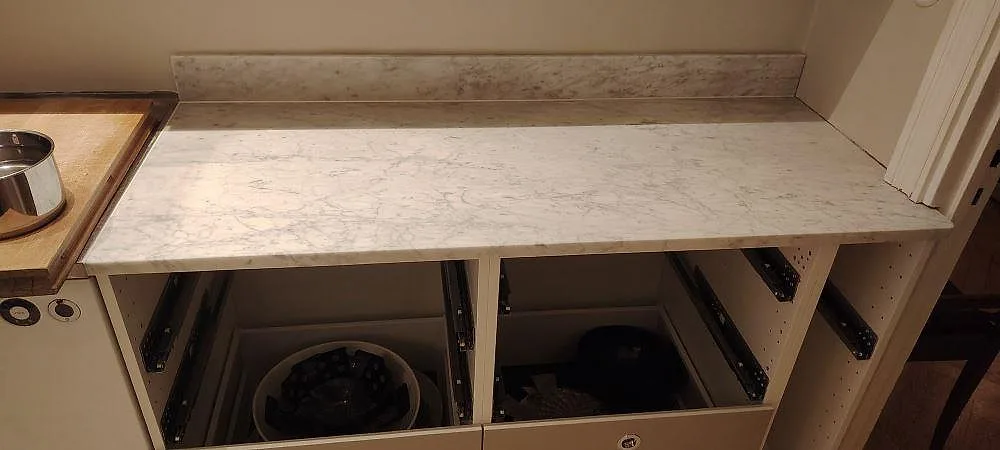 Køkkenbordplade i mat Carrara C marmor med låg stänkkant og grå åretegning på öppna köksstommar i Stockholm.