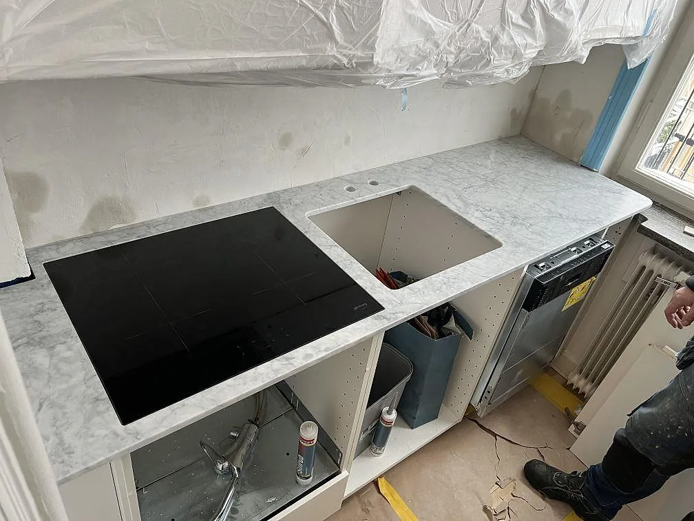Køkkenbordplade i mat Carrara C-marmor med sort kogeplade, udskæring for vask og Armaturhul i ett køkken i Stockholm.