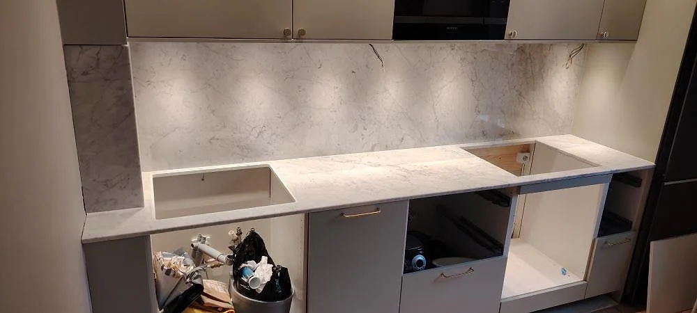Køkkenbordplade i poleret Carrara C-marmor, 20 mm, med marmorklädd væg og synlig diskhourtagning i ett køkken under montering i Stockholm.