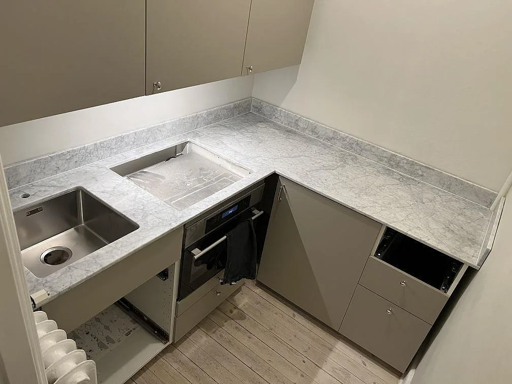 Køkkenbordplade i mat Carrara C marmor med rostfri vask, hällöppning og uppvikt stänkkant i ett vinkelkök i Stockholm.