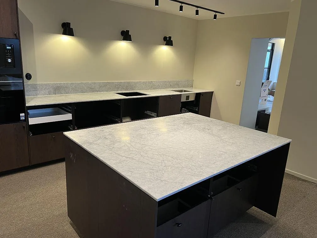Køkkenbordplade i mat Carrara C marmor med stor køkkenø, lige väggbänk og låg stänkkant i ett køkken i Stockholm.