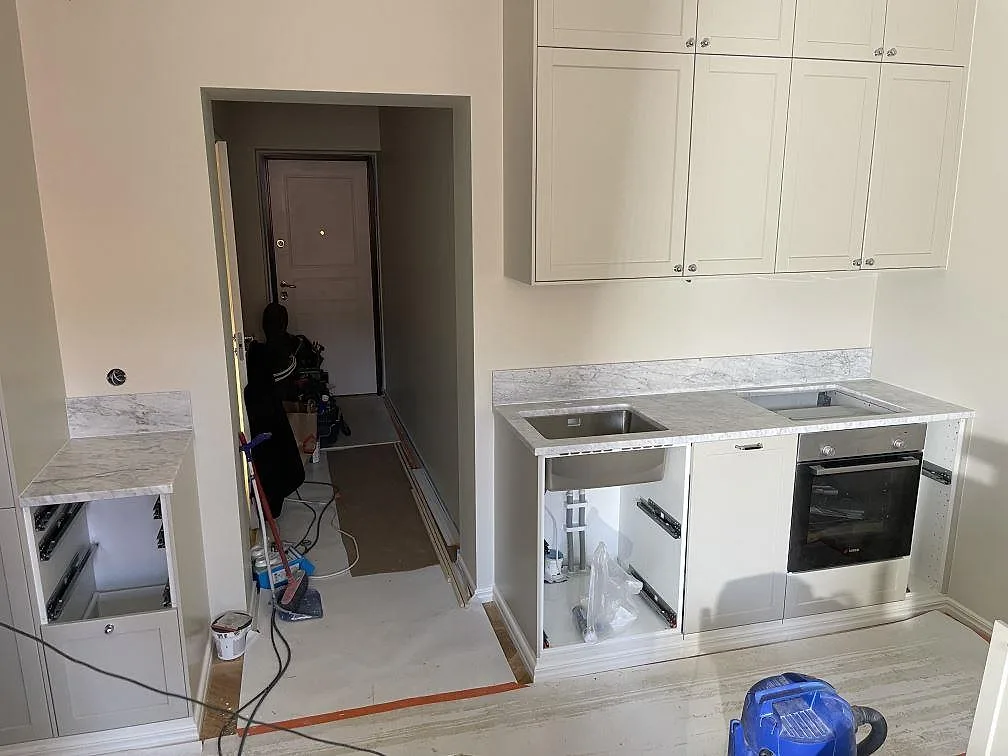 Køkkenbordplade i Carrara C marmor, mat, med låg stänkkant, vask og hällöppning i ett køkken under montering i Stockholm.