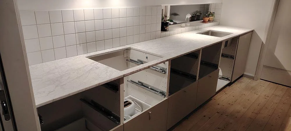 Køkkenbordplade i mat Carrara C marmor, 20 mm, på lang bänkrad med kakel, vask og hällöppning i Stocksund.