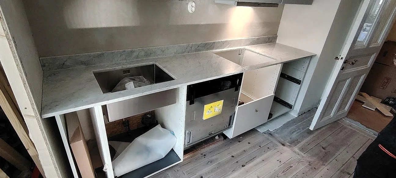 Køkkenbordplade i Carrara C marmor, poleret, med vask og låg stänkkant i ett køkken under montering i Sundbyberg.