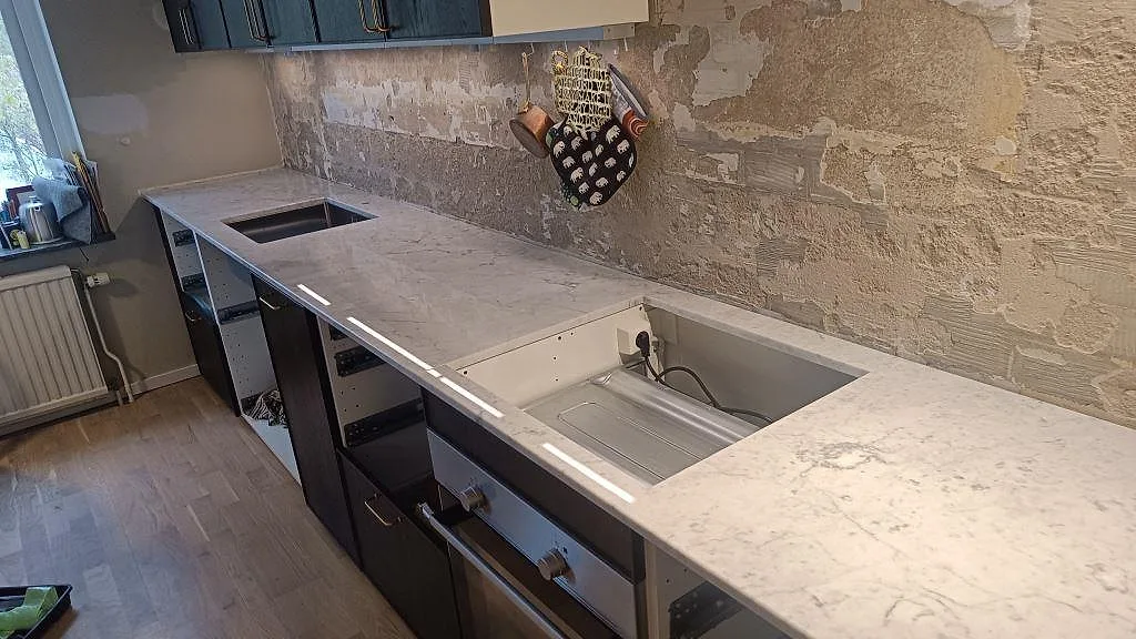 Køkkenbordplade i poleret Carrara C marmor med lange bänkytor og öppna köksstommar under montering i Västra Frölunda.