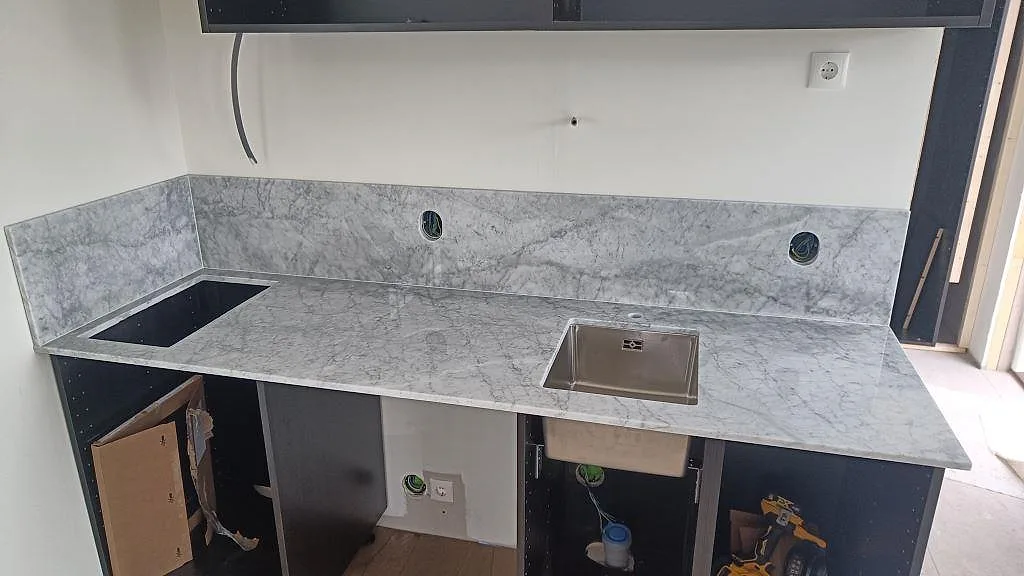 Køkkenbordplade i poleret Carrara C marmor med stänkkant, vask og hällöppning i ett køkken under montering i Västra Karup.