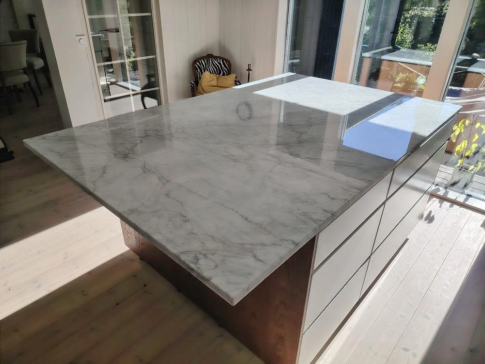 Poleret køkkenø og Bordplade i Carrara C marmor, 30 mm, med tyk kant og grå åretegning i ett fönsterljust køkken i Vaxholm.