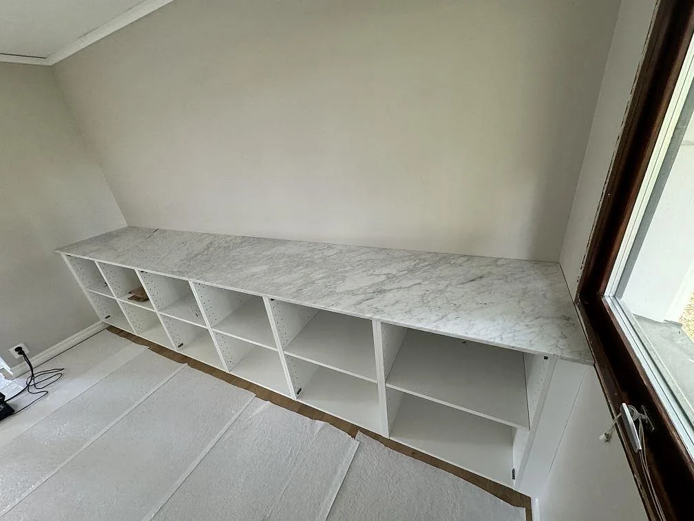 Mat køkkenbordplade i Carrara C marmor over vita öppna skabe i ett køkken i Klippan.