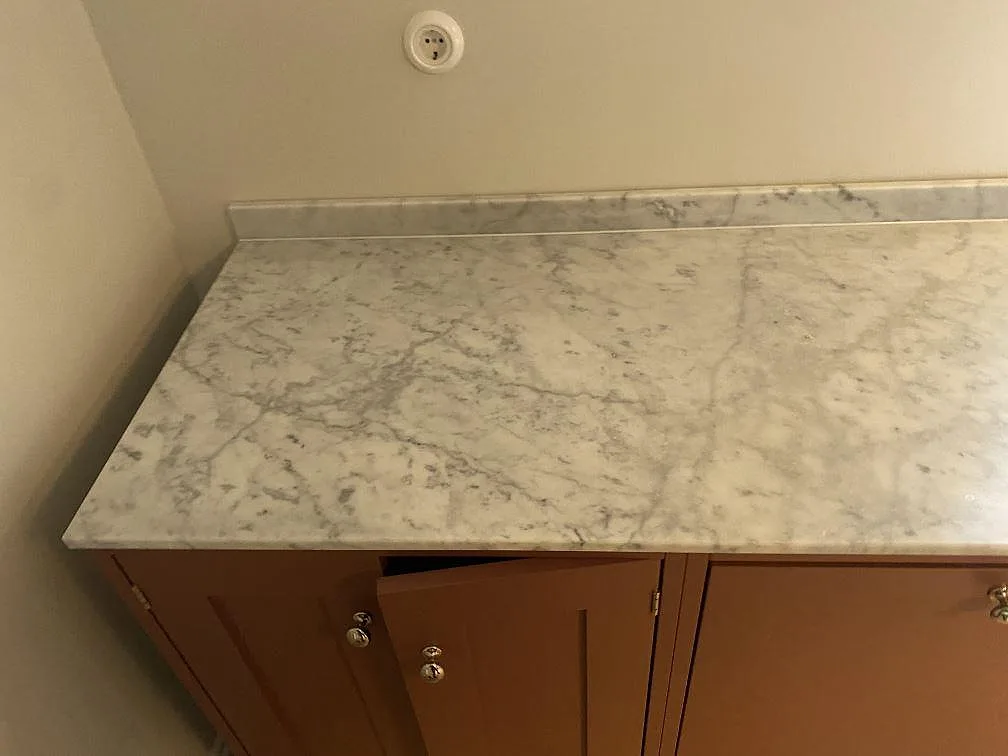 Køkkenbordplade i mat Carrara CD-marmor med uppvikt stänkkant på terrakottafärgade köksstommar i ett køkken i Limhamn.