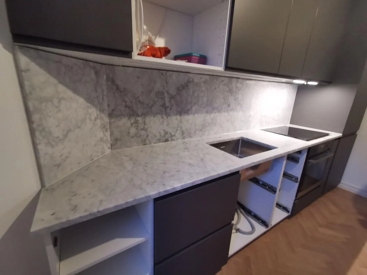 Køkkenbordplade i hvid Carrara CD-marmor, mat, med heltäckande stänkvägg i samme marmor, underlimmad rostfri vask og övermonterad induktionshäll i ett køkken i Malmö.