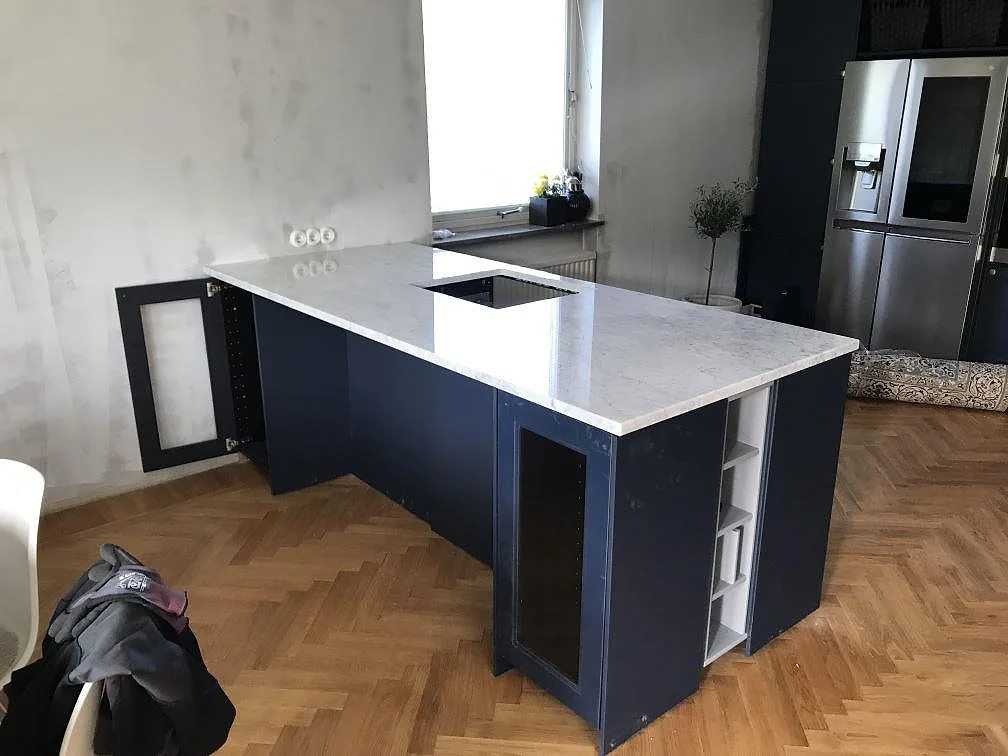 Køkkenbordplade i hvid Carrara CD marmor med grå åretegning monteret på en marinblå halvö i ett køkken under montering i Malmö.