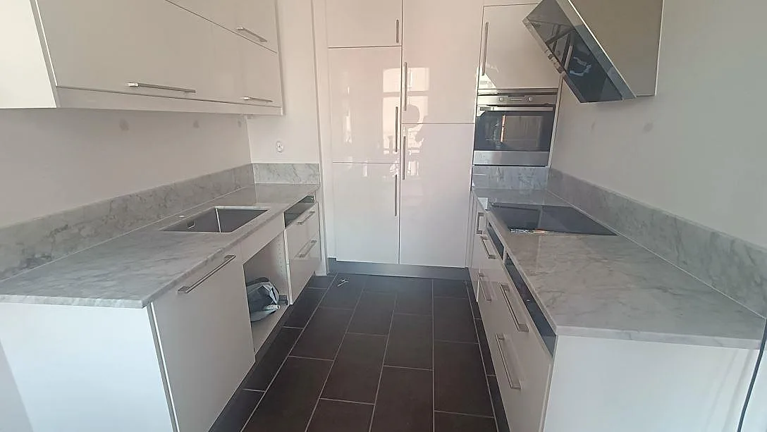 Køkkenbordplade i hvid Carrara CD-marmor, poleret, med grå åretegning längs båda bänkraderna i ett køkken i Malmö.