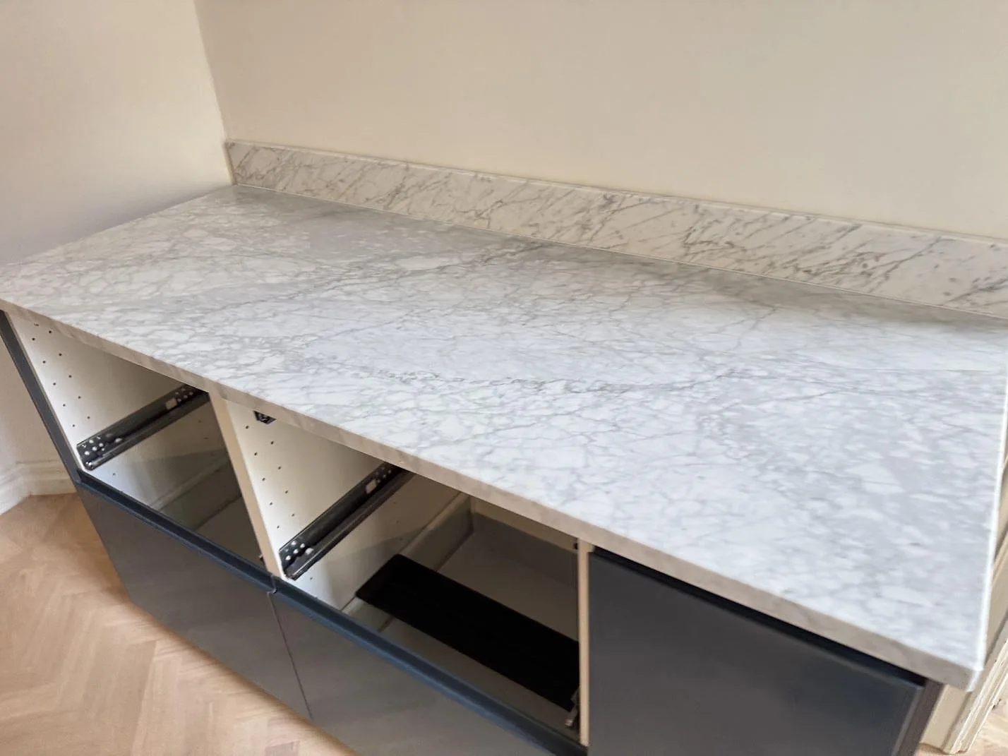 Bordplade i mat Carrara C-marmor med uppvikt stänkkant på mørke skåpstommar i Malmö.