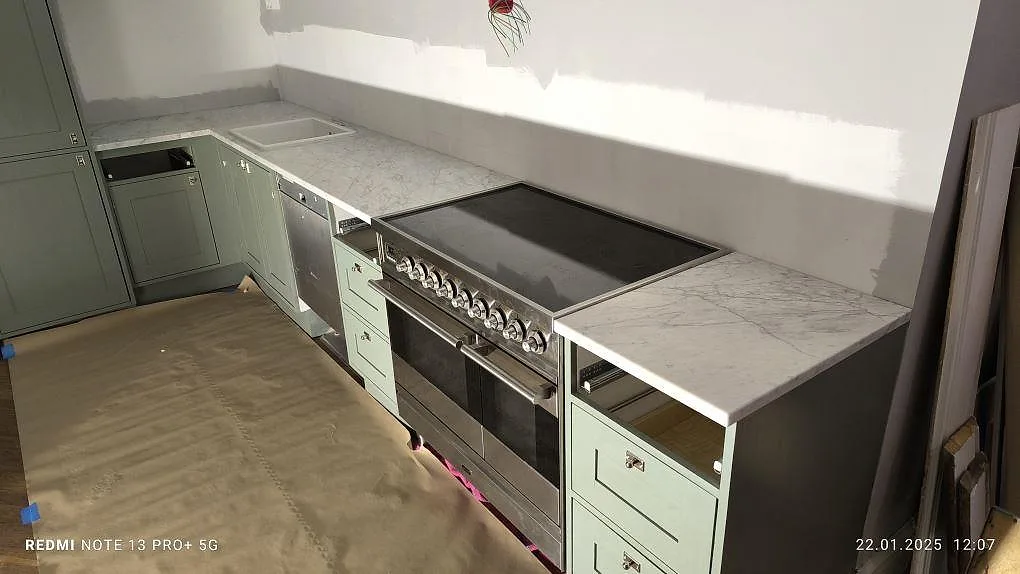 Mat køkkenbordplade i 20 mm Carrara C marmor på en lang köksrad med fristående komfur i Stockholm.