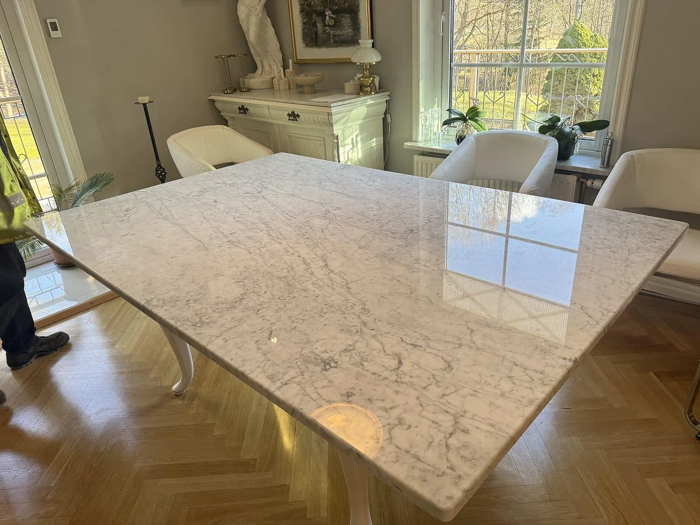 Bordsskiva i poleret Carrara C marmor med grå åretegning, placerad som matbord i ett ljust rum i Svenshögen.