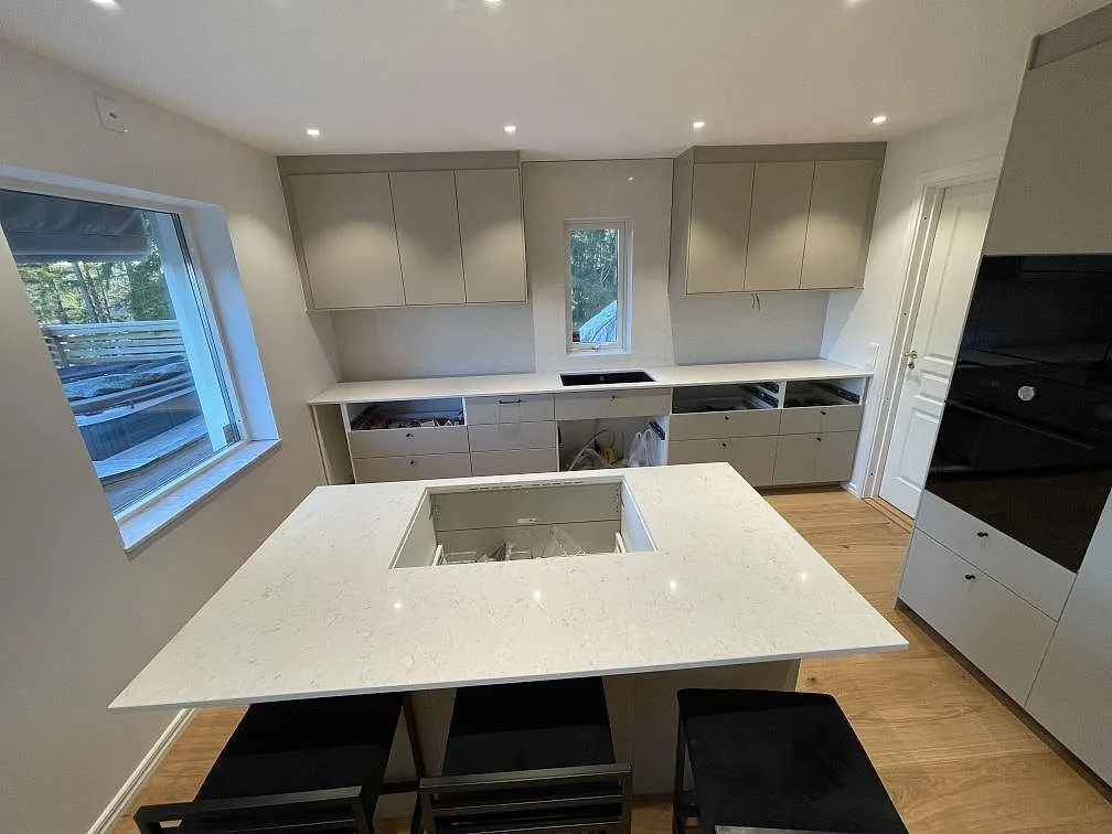 Køkkenø i mat Carrara C-marmor, med lys bakre bänkrad i Silestone Snowy Ibiza og förberedd kogeplade i ett køkken under montering i Uttran.