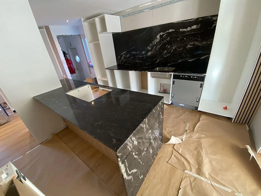 Køkkenbordplade i sort Cosmic Black granit, poleret, med køkkenø og heltäckande stänkvägg i samme sten i ett køkken under montering i Kävlinge.