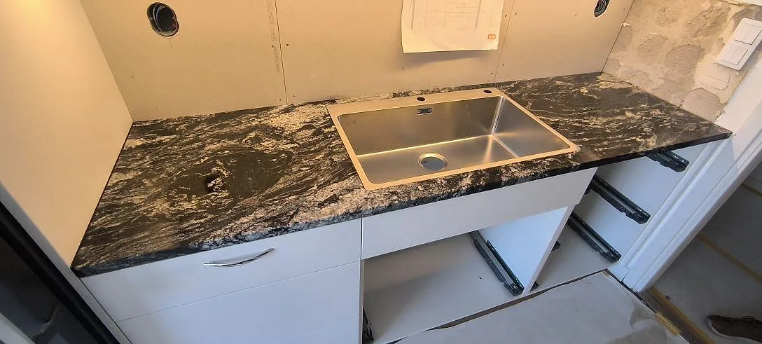 Køkkenbordplade i poleret Cosmic Black granit med synlig vask og kraftig lys åretegning i ett køkken i Uppsala.