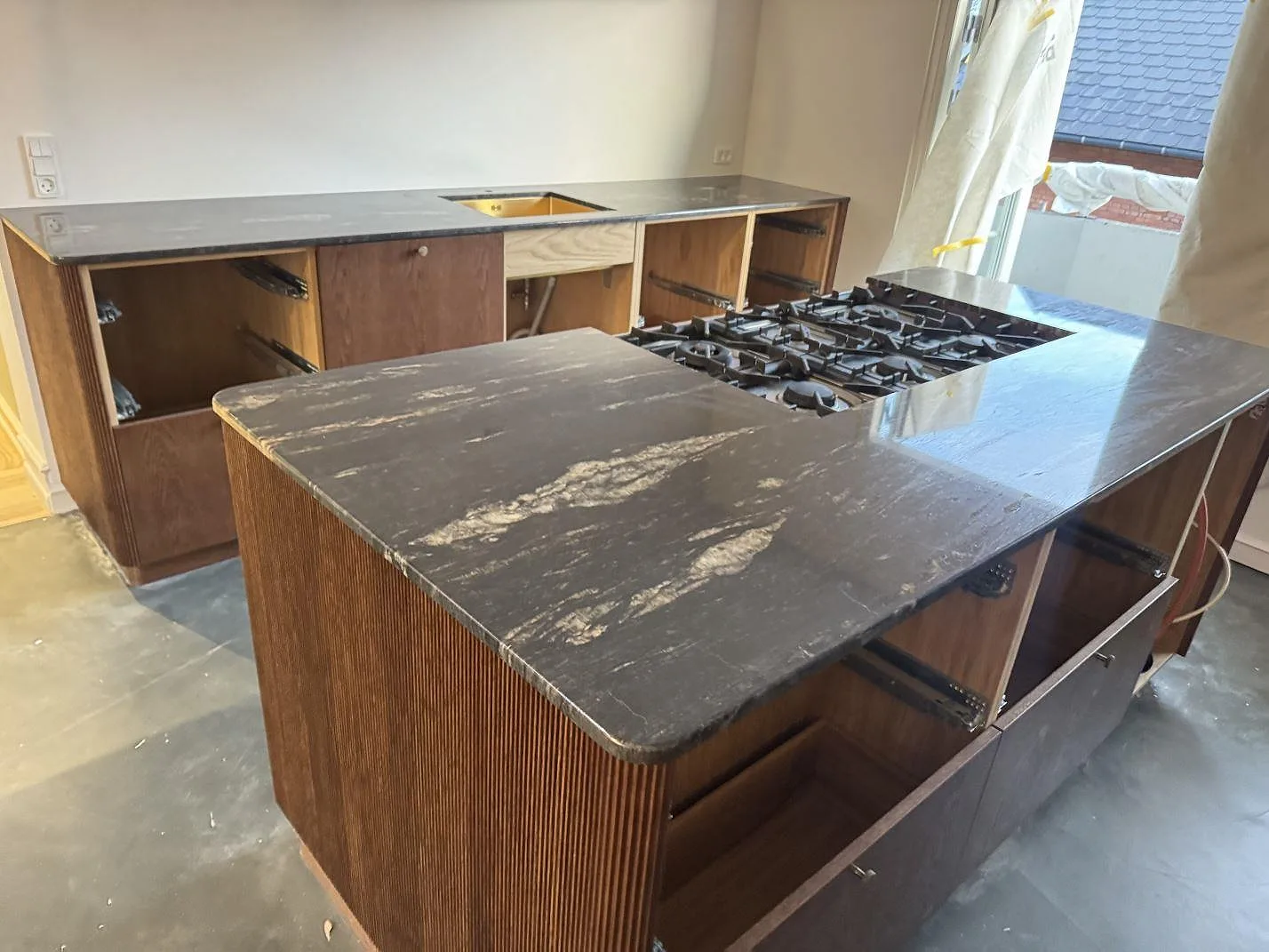 Køkkenbordplade og køkkenø i poleret Cosmic Black granit med lys åretegning, monterade på trästommar i ett køkken i Valby.